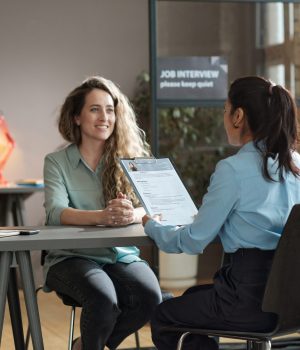 Rear view of young woman presenting her resume to director while sitting with her at table during job interview